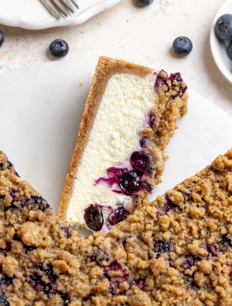 Delicious slice of blueberry crumble cheesecake topped with crumbs and fresh blueberries
